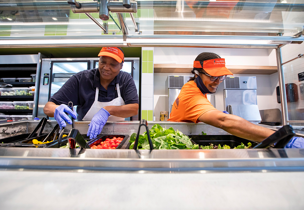 The Dining Services staff is shown smiling and hard at work with lots of fresh vegetables in front of them.