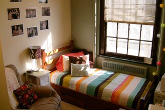Single room with bed, window, side table, chair, and decorations