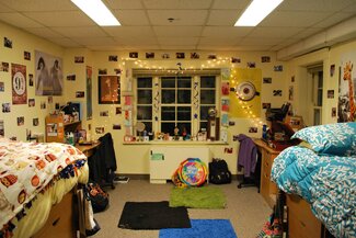 Double room with two beds, two desks, two rolling chairs, string lights, pictures on the wall, large window, colorful decorations