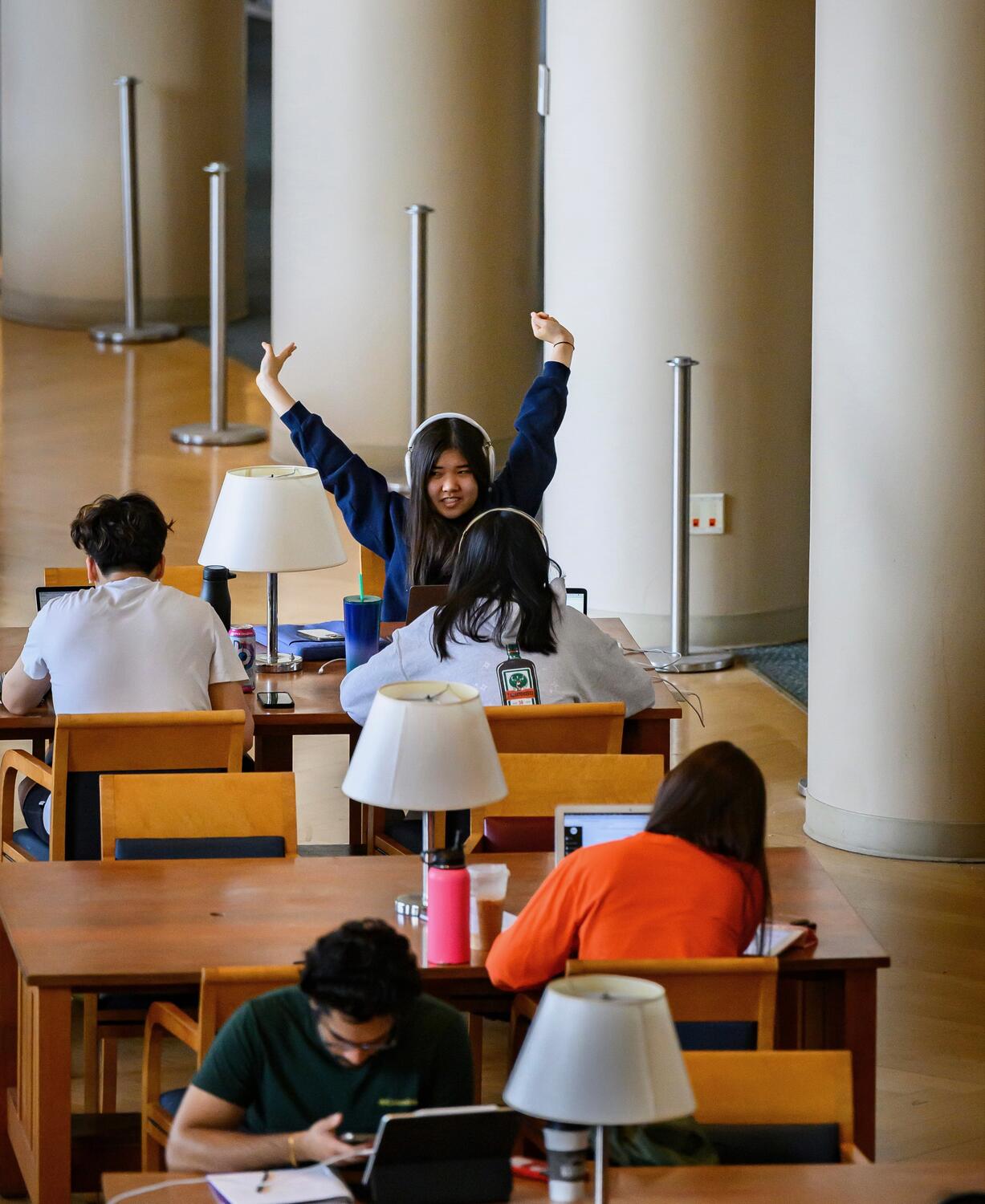 A group of students study in a common space, with one student yawning and stretching.